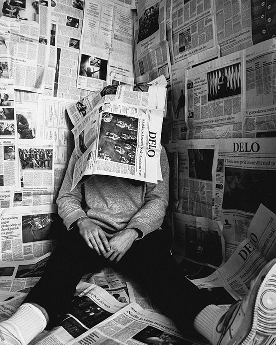 man sitting in room with newspapers and newspaper on his head